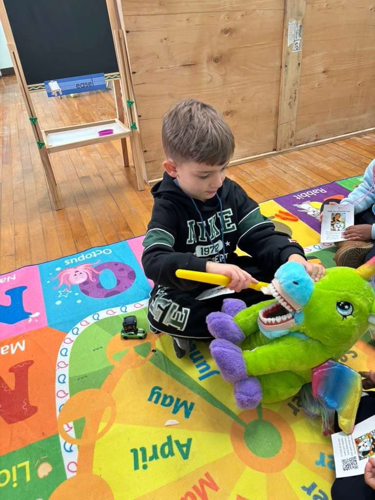 A child practices brushing teeth on a soft toy with an oversized toothbrush.
