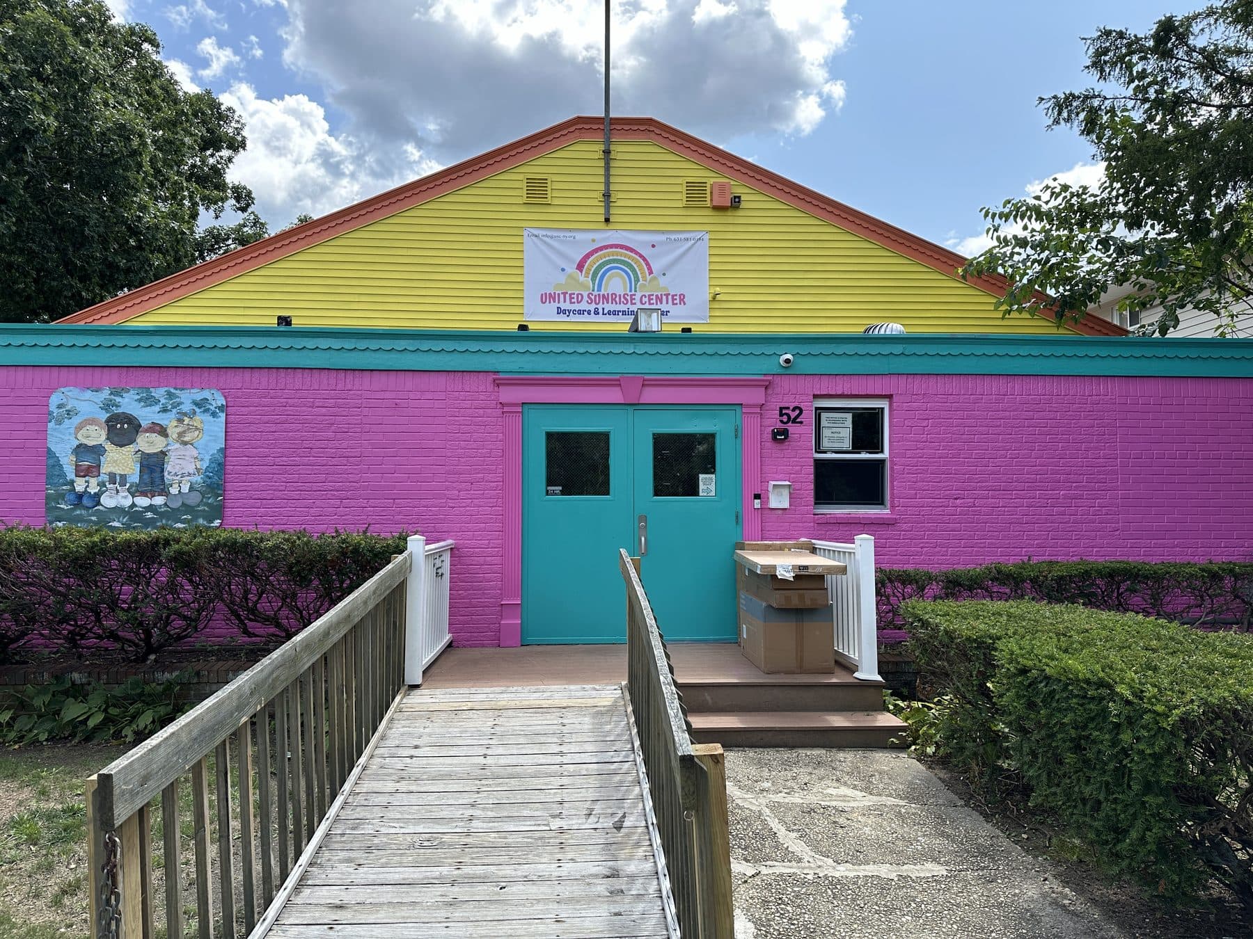 The United Sunrise Center building in East Islip: a pink and yellow single-storey school with a rainbow sign and a ramp to the teal front doors.